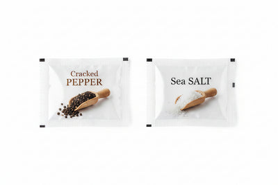 Two packets of cracked pepper and sea salt on a white background