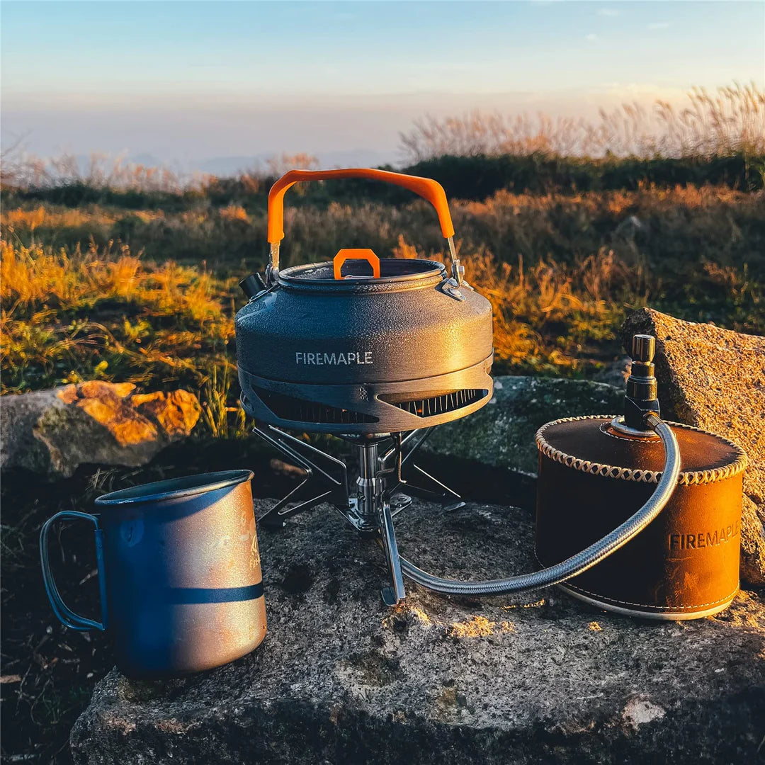 Camp stove with kettle and fuel canister on a rock in a natural setting