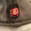 Close-up of a gray cap with a embroidered emblem featuring red, gold, and black colors.