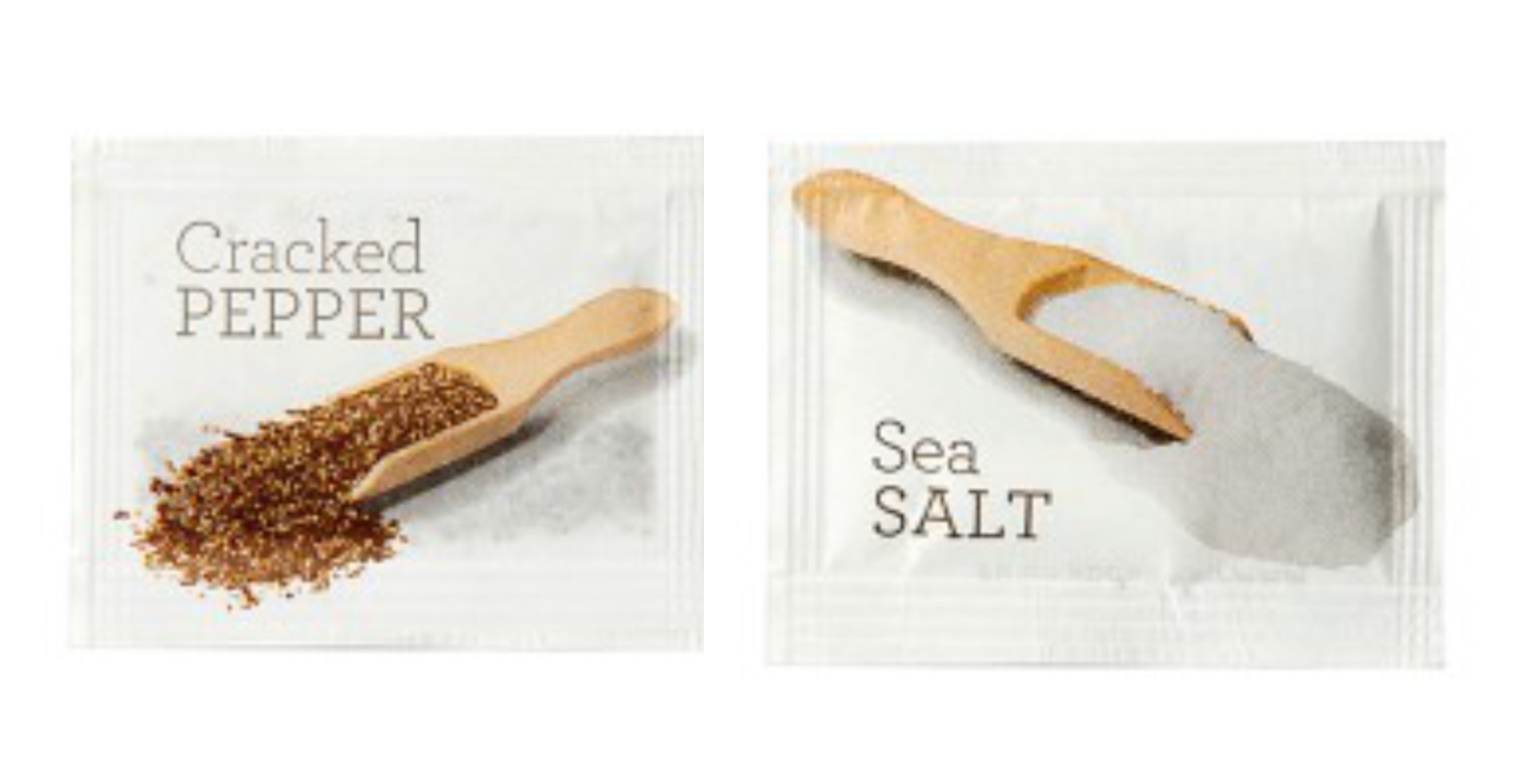 Two single serve packets, one labeled 'Cracked PEPPER' with a wooden spoonful of pepper next to it, and the other labeled 'Sea SALT' with a scoop of salt.