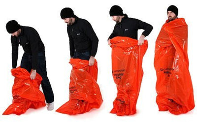 A series of four images showing a person wearing black clothing interacting with a bright orange emergency survival bag. The images depict the bag being packed and unfolded.